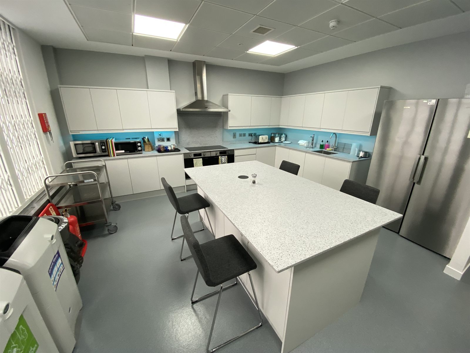 Refurbished staff kitchen with handleless units, stone-effect island and integrated appliances